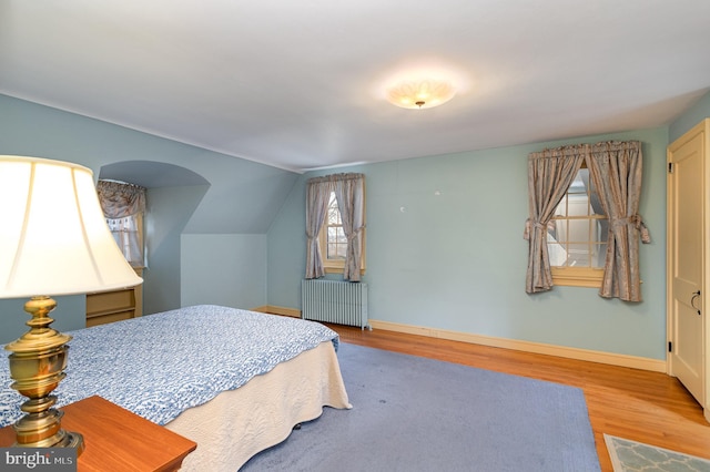 bedroom with lofted ceiling, radiator, wood finished floors, and baseboards