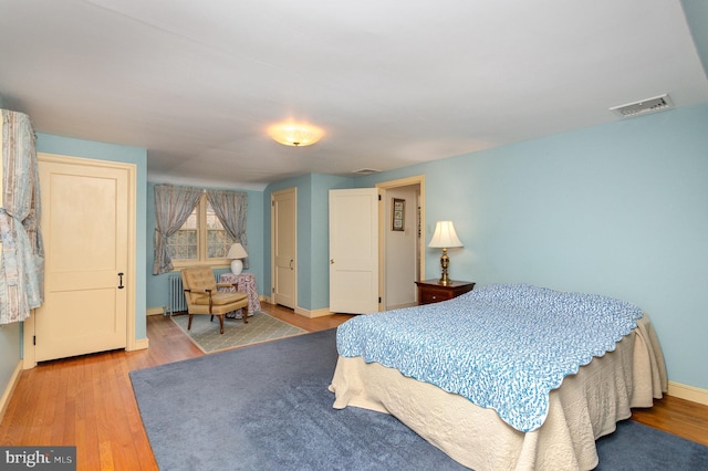 bedroom featuring visible vents, radiator, baseboards, and wood finished floors