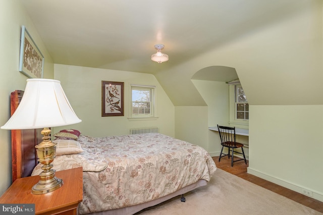 bedroom featuring radiator, baseboards, lofted ceiling, and wood finished floors