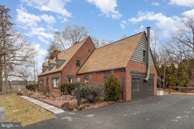 view of property exterior featuring brick siding, roof with shingles, and a chimney