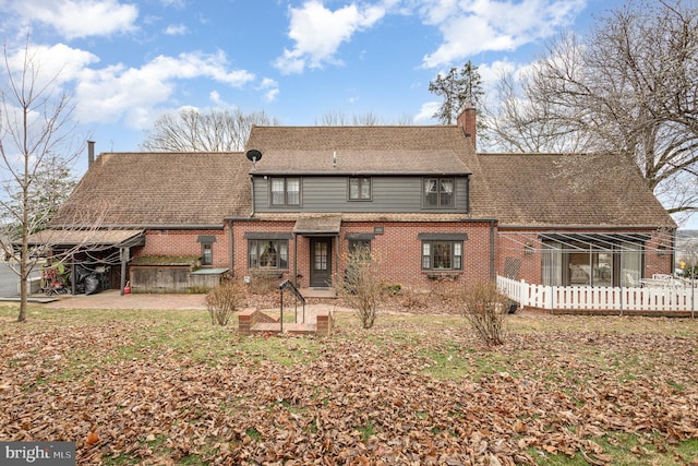 rear view of house featuring a patio, brick siding, a chimney, and a shingled roof