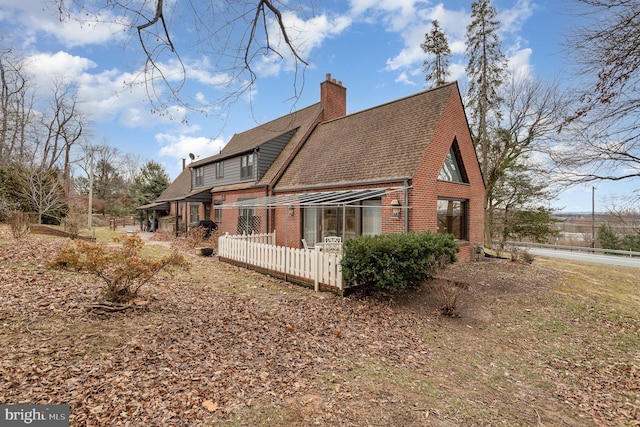 rear view of property with brick siding, a chimney, and a shingled roof