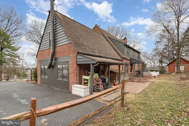 back of property with brick siding, a chimney, a shingled roof, and a yard