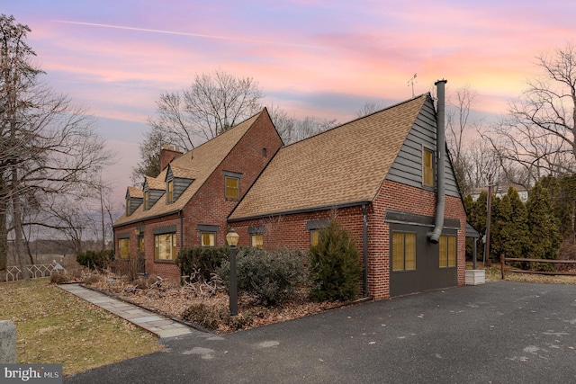 view of property exterior featuring brick siding, a chimney, and a shingled roof