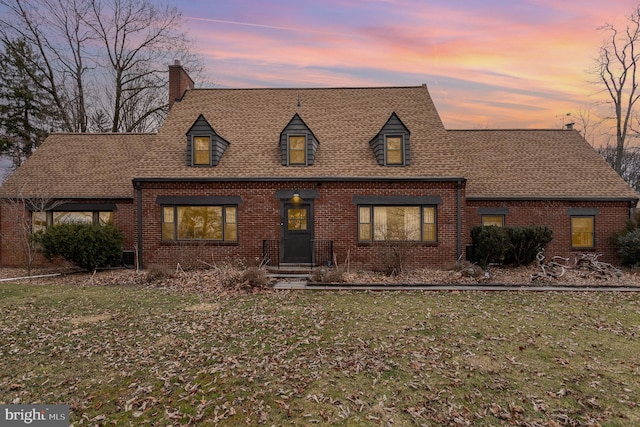 cape cod-style house featuring brick siding, a shingled roof, and a front yard