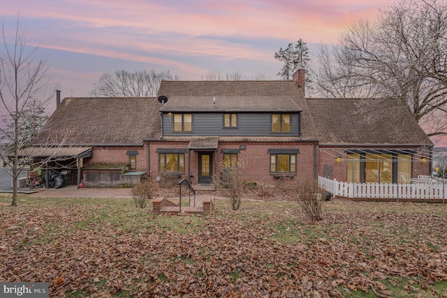 back of property featuring brick siding, a patio area, a chimney, and a shingled roof