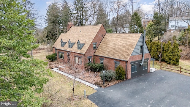 view of property exterior with driveway, brick siding, a chimney, and fence