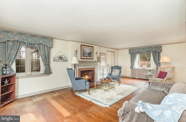 living area with visible vents, baseboards, ornamental molding, wood-type flooring, and a brick fireplace