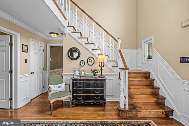 stairs with a wainscoted wall, wood finished floors, ornamental molding, and a decorative wall