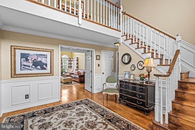 foyer featuring crown molding, stairway, wainscoting, a towering ceiling, and wood finished floors