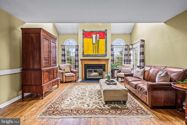 living area featuring a wealth of natural light, a glass covered fireplace, light wood finished floors, and baseboards