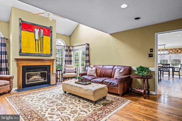 living room featuring a fireplace with flush hearth, lofted ceiling, baseboards, and wood finished floors