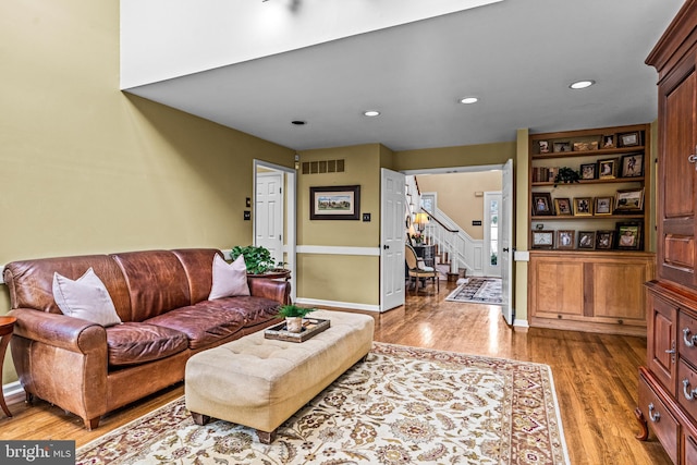 living area with recessed lighting, visible vents, wood finished floors, and stairs