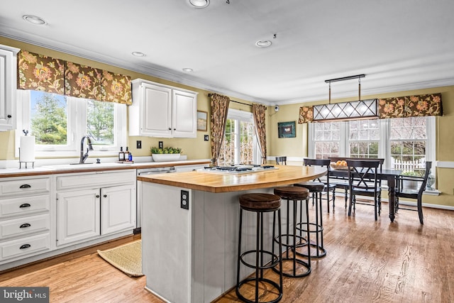 kitchen with butcher block countertops, ornamental molding, a kitchen bar, and a sink