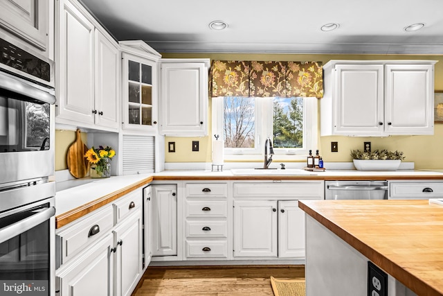 kitchen with butcher block countertops, white cabinets, stainless steel appliances, and a sink