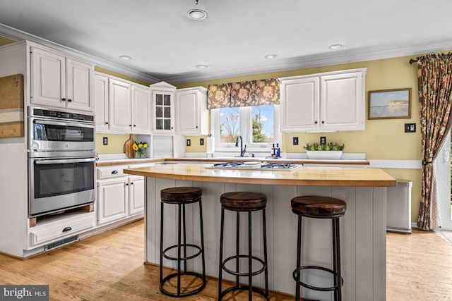 kitchen with white cabinetry, ornamental molding, stainless steel double oven, and wood counters