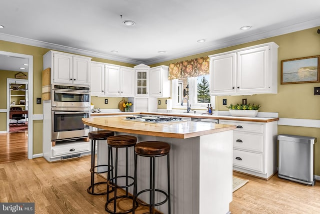 kitchen featuring a kitchen breakfast bar, white cabinets, light wood-style flooring, and appliances with stainless steel finishes