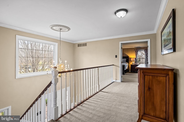 hall with a notable chandelier, carpet flooring, crown molding, and visible vents