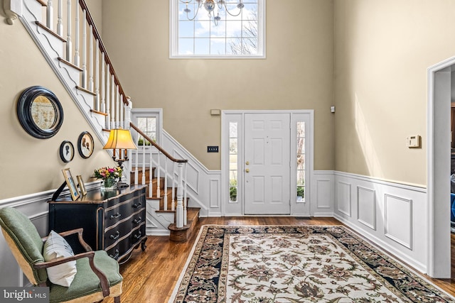 entrance foyer with stairway, wood finished floors, a wainscoted wall, and a towering ceiling