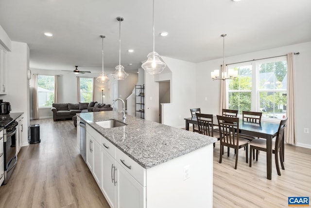 kitchen with a sink, a center island with sink, range with gas stovetop, light wood-style floors, and stainless steel dishwasher