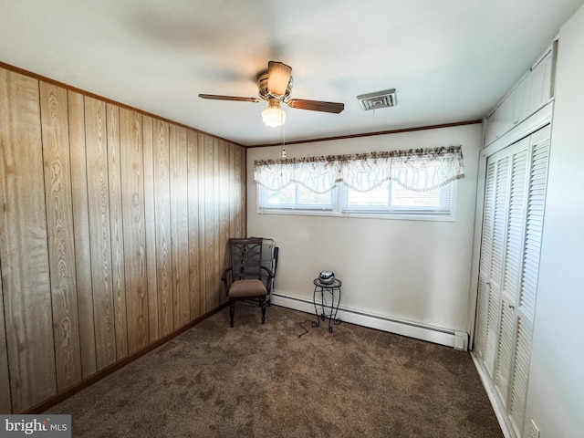 unfurnished room with visible vents, wooden walls, baseboard heating, and carpet flooring