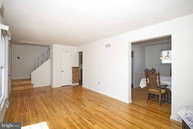 living area featuring stairway, visible vents, light wood finished floors, and a notable chandelier