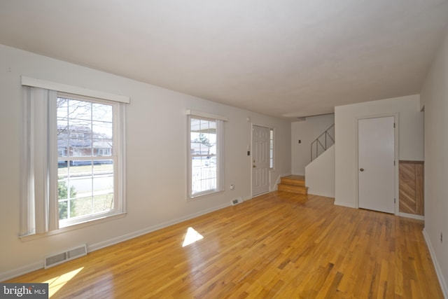 unfurnished living room featuring stairs, light wood finished floors, plenty of natural light, and visible vents