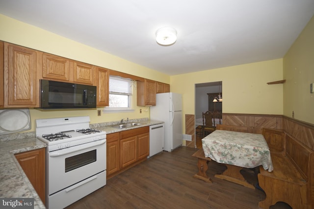 kitchen with a wainscoted wall, dark wood-type flooring, a sink, light stone countertops, and white appliances