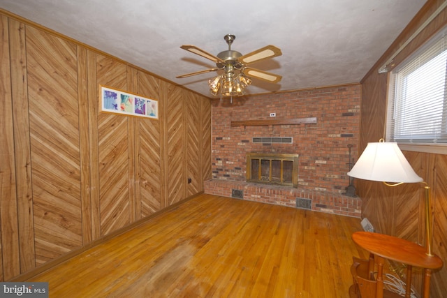 unfurnished living room featuring a fireplace, visible vents, ornamental molding, wood walls, and wood finished floors