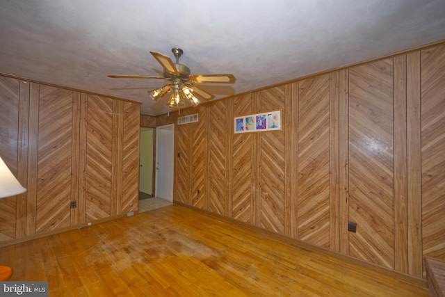 spare room with ceiling fan, hardwood / wood-style flooring, visible vents, and wooden walls