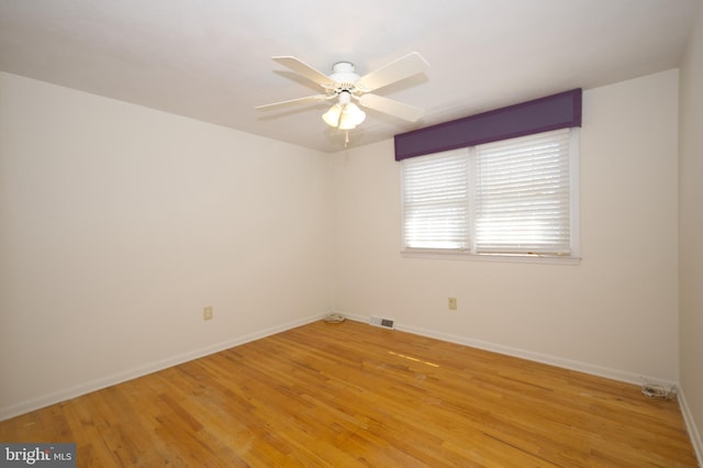 spare room featuring light wood finished floors, baseboards, visible vents, and ceiling fan