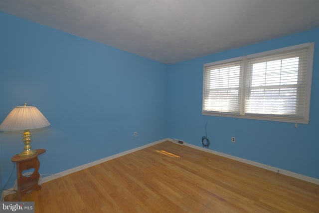 empty room with baseboards, visible vents, and light wood finished floors