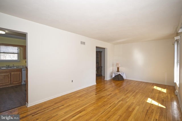 unfurnished room with light wood-type flooring, baseboards, visible vents, and a sink