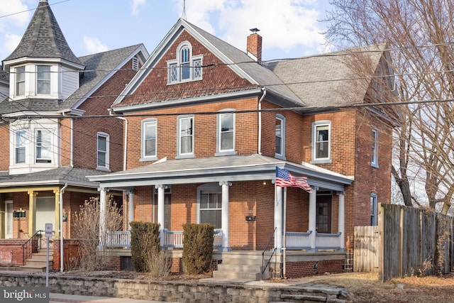 victorian house with brick siding, fence, covered porch, and a chimney