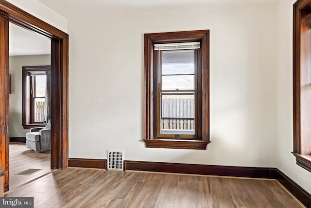 empty room featuring wood finished floors, visible vents, and baseboards