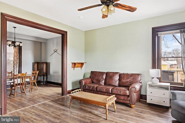 living area with ceiling fan with notable chandelier, baseboards, and wood finished floors