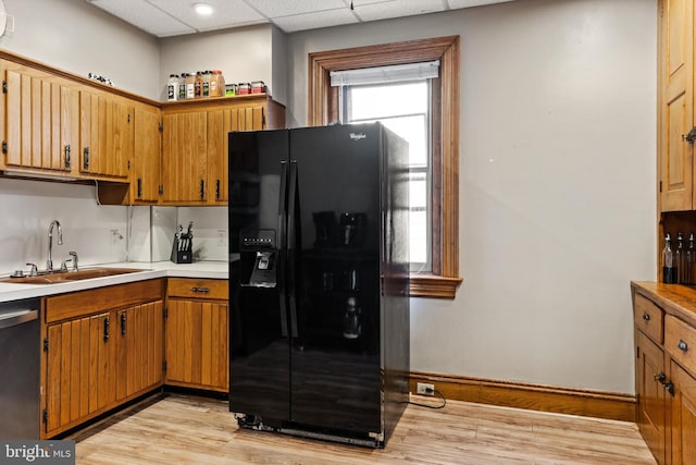 kitchen featuring light wood-type flooring, a sink, a drop ceiling, black fridge with ice dispenser, and stainless steel dishwasher