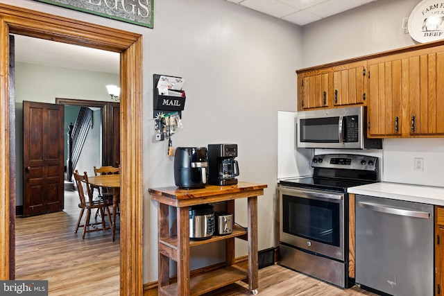 kitchen with light wood-type flooring, brown cabinets, stainless steel appliances, light countertops, and a paneled ceiling