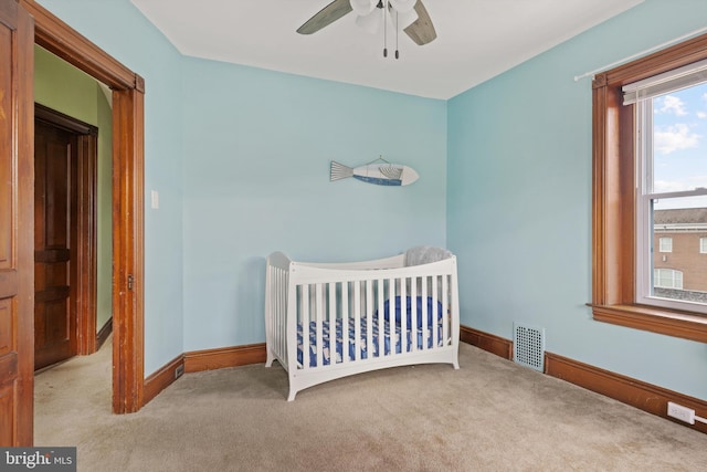 carpeted bedroom with visible vents, baseboards, a nursery area, and ceiling fan