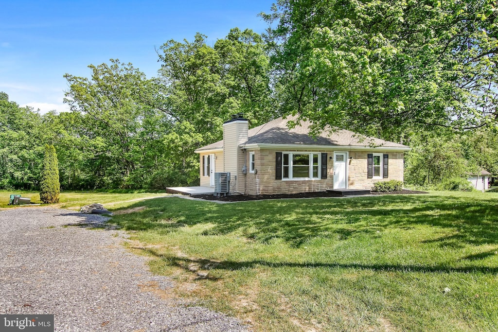 view of front facade with a front yard, stone siding, central AC, and a chimney