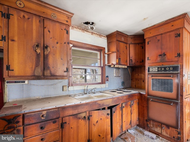 kitchen featuring a sink, brown cabinets, backsplash, and oven