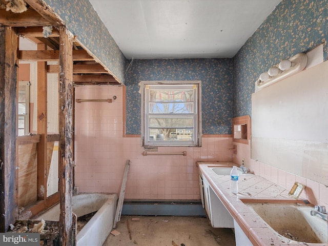 full bath with a sink, a wainscoted wall, a tub to relax in, and wallpapered walls