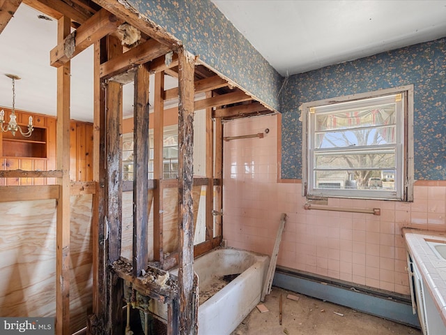 bathroom with wallpapered walls, a chandelier, baseboard heating, wainscoting, and tile walls