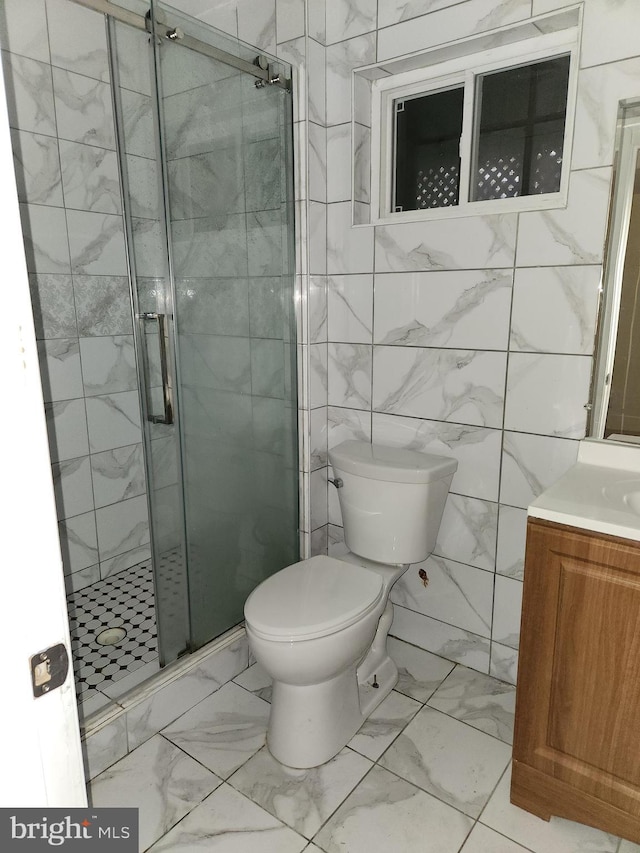 bathroom featuring toilet, marble finish floor, vanity, a shower stall, and tile walls