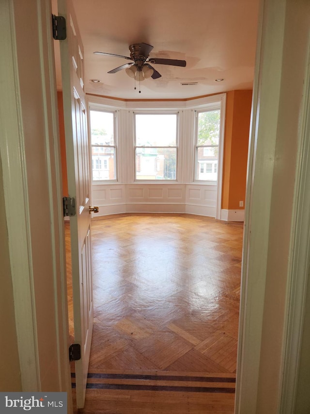 empty room with a ceiling fan, a healthy amount of sunlight, a decorative wall, and visible vents