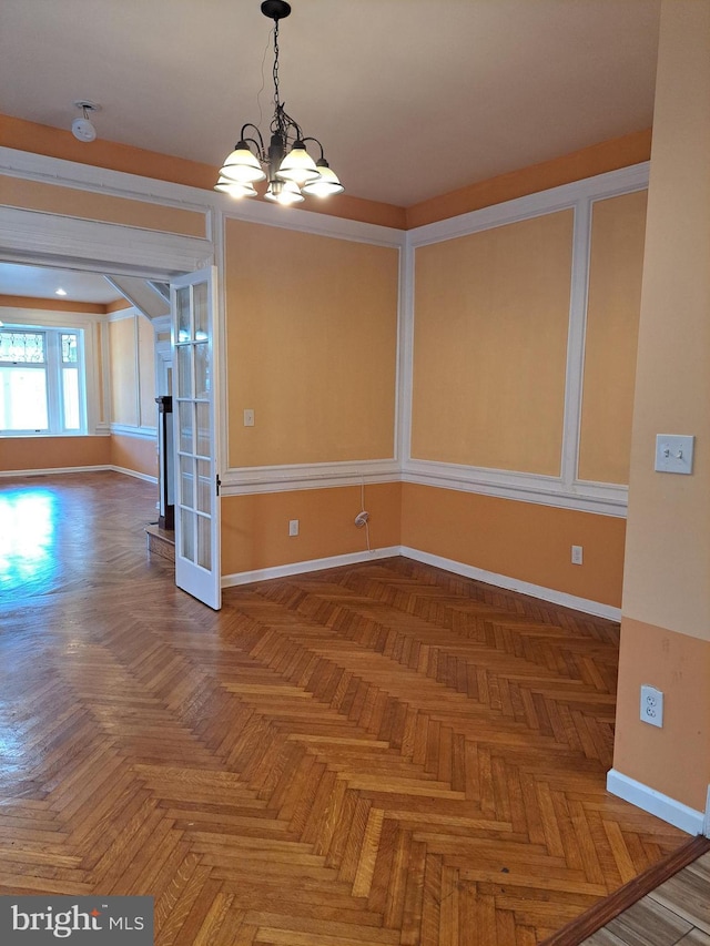 unfurnished dining area featuring baseboards, arched walkways, and a notable chandelier