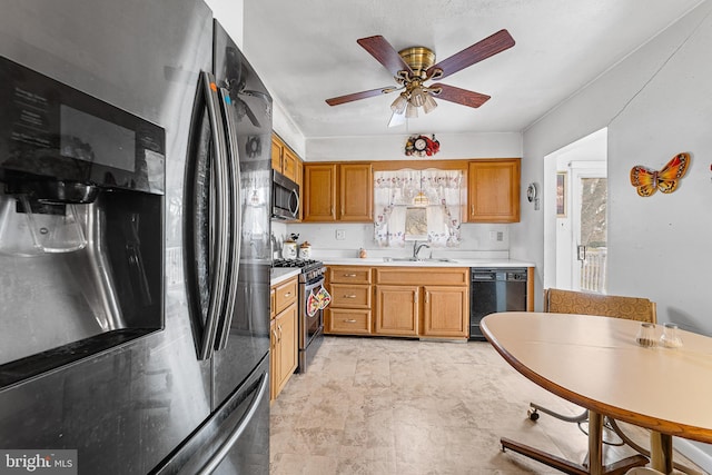 kitchen featuring a ceiling fan, brown cabinetry, a sink, light countertops, and appliances with stainless steel finishes