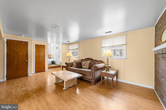 living area featuring visible vents, light wood-style flooring, a brick fireplace, and baseboards