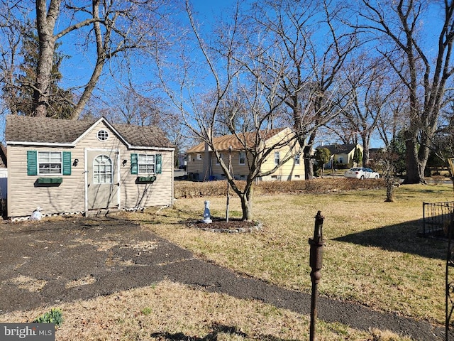 view of front of house featuring an outbuilding, a shingled roof, and a front lawn