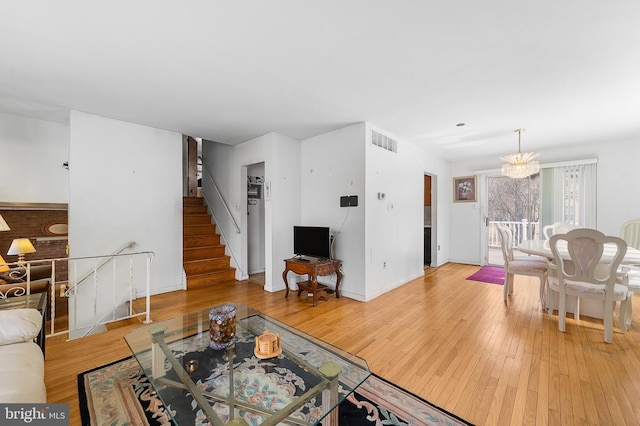 living area with visible vents, wood-type flooring, baseboards, a chandelier, and stairs